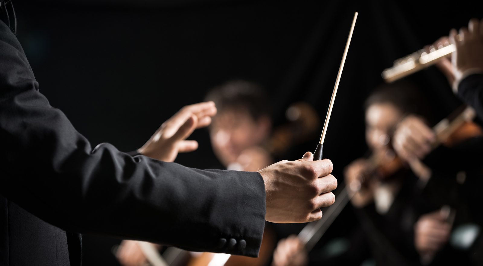 Conductor directing symphony orchestra with performers on background hands close-up.